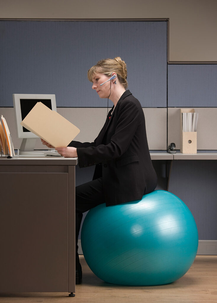 Office worker sitting on balance ball while working at her desk.