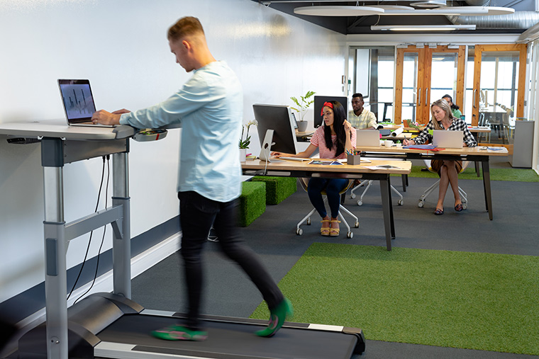 Office worker walking on treadmill desk while working on his laptop