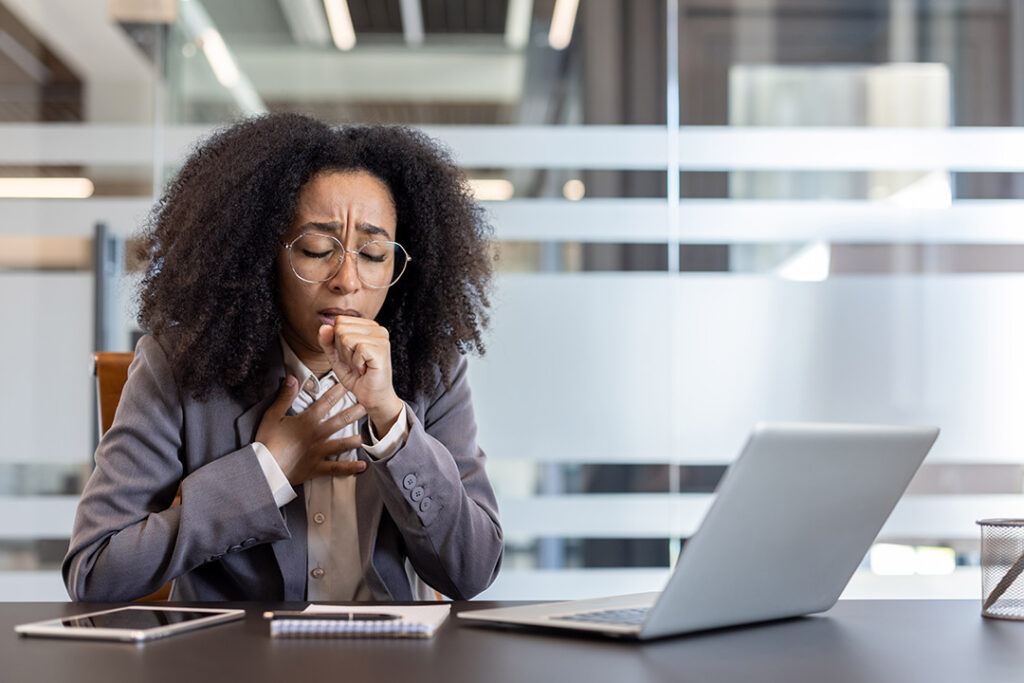 Businesswoman suffering from asthma attack and coughing behind her workplace in the office.